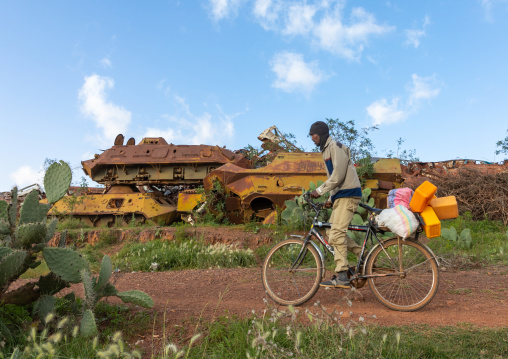 Eritrean man riding a bicycle in front of the military tank graveyard, Central region, Asmara, Eritrea