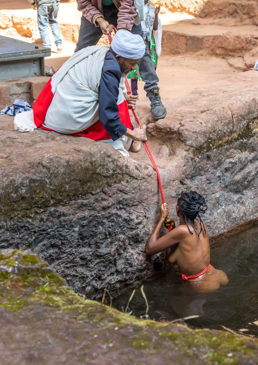 Ethiopian priest helping a woman to take a bath in holy water to fight her infertility, Amhara Region, Lalibela, Ethiopia