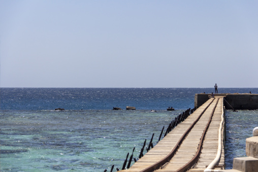A wooden pier extends into the turquoise lagoon enclosed by Sanganeb reef, Red Sea State, Sanganeb, Sudan