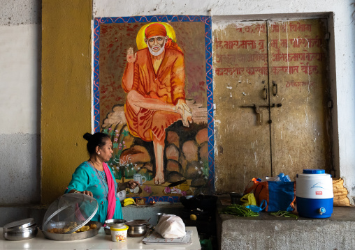 Indian woman preparing food in the street under a guru mural, Maharashtra state, Mumbai, India