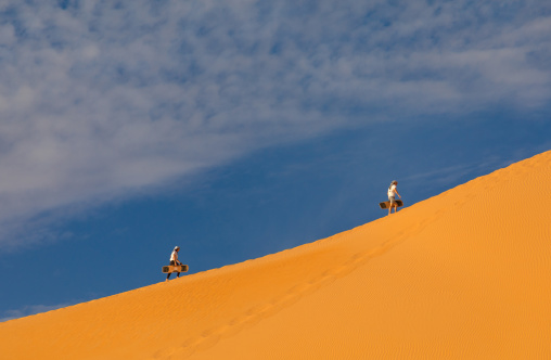Group of friends climbing a dune to sandboard in Rub al Khali desert, Najran Province, Thar, Saudi Arabia