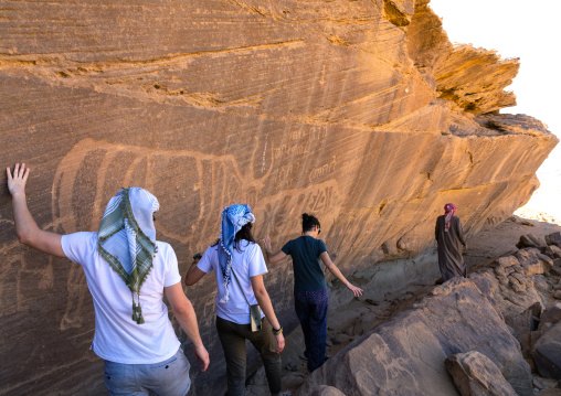 Tourists passing in front of petroglyphs on a rock depicting cows, Najran Province, Thar, Saudi Arabia