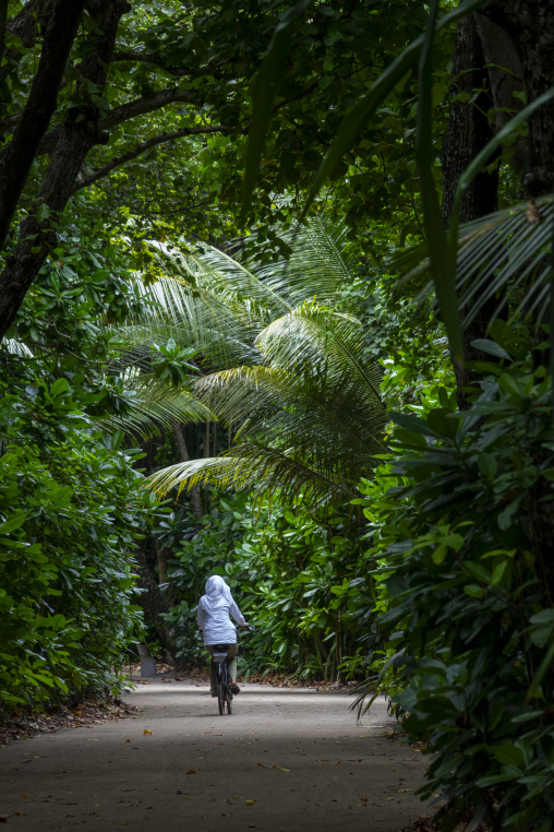 A woman rides a bicycle along a shaded jungle path, Baa Atoll, Soneva Fushi, Maldives