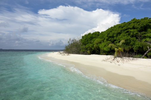 A narrow sandbank curves along clear turquoise water toward a distant island, Baa Atoll, Soneva Fushi, Maldives