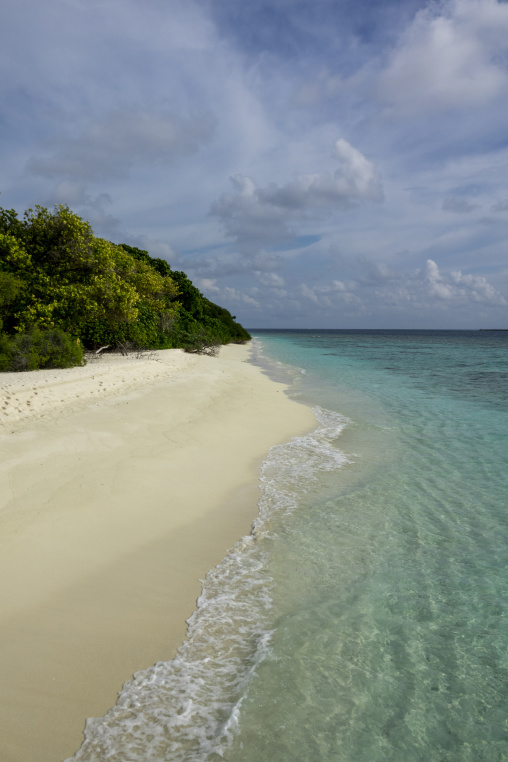 Footprints trail across a deserted white sand beach beside the turquoise sea, Baa Atoll, Soneva Fushi, Maldives