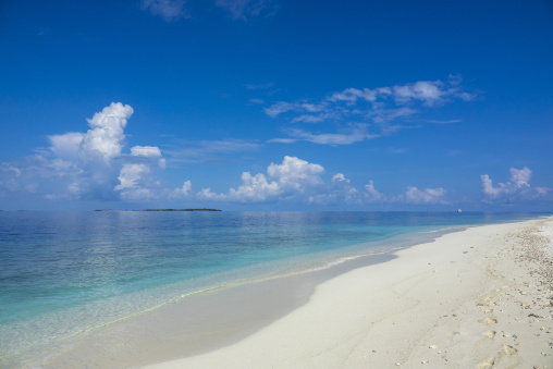 Footprints lead along a white sand beach overlooking a calm turquoise lagoon and distant island, Baa Atoll, Soneva Fushi, Maldives