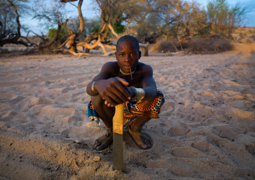 Mucubal tribe man with his machete sit in a dry river, Namibe Province, Virei, Angola