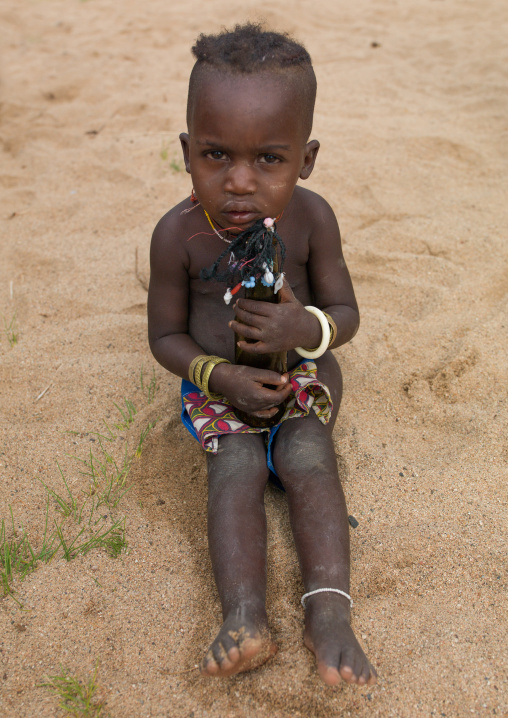 Mucubal tribe boy holding a doll made with a bottle beer, Namibe Province, Virei, Angola