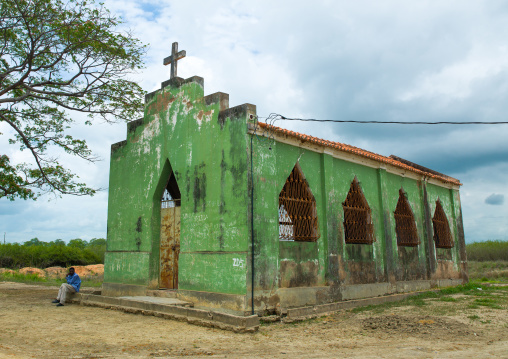 Angolan man sit in front of an abandoned green church, Malanje Province, Calandula, Angola