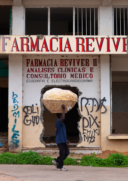 Angolan man carrying a huge basket on his head in front of a pharmacy, Huambo Province, Huambo, Angola