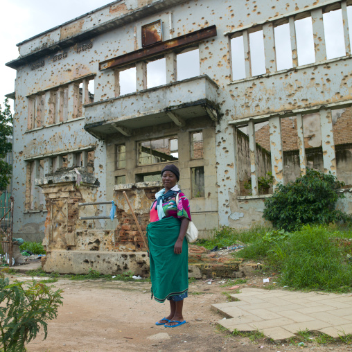 Woman In Front Of A Building Facade In Ruins Riddled With Bullet Impacts, Huambo, Angola