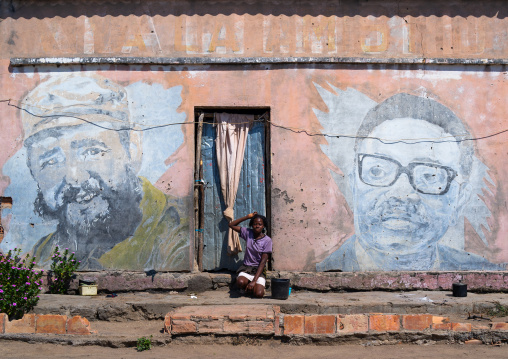 Woman in front of an old propaganda wall painting with Fidel Castro and Jose Eduardo dos Santos, Cunene Province, Cahama, Angola