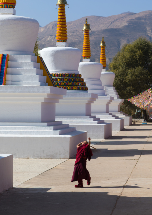 Young tibetan monk playing between the stupas in Wutun si monastery, Qinghai province, Wutun, China