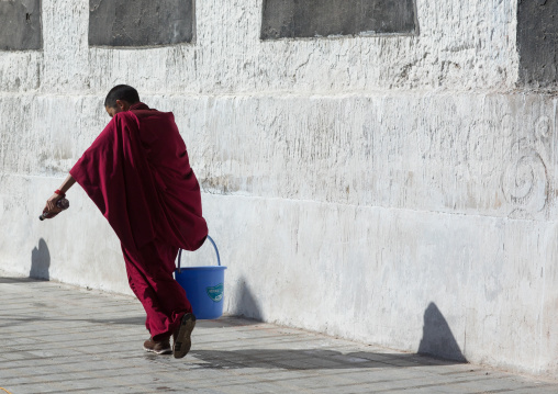 Tibetan monk carrying bucket for the painting of a temple in Rongwo monastery, Tongren County, Longwu, China