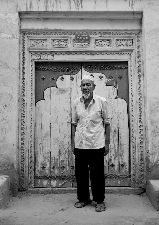 Old Uyghur Man In Front Of A Traditional Door In Old Town, Keriya, Xinjiang Uyghur Autonomous Region, China