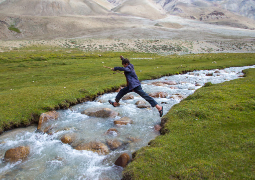 Wakhi boy jumping over a river in pamir mountains, Big pamir, Wakhan, Afghanistan