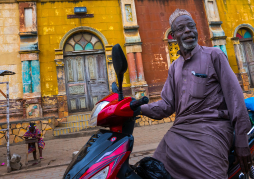 Benin, West Africa, Porto-Novo, old muslim man on a scooter in front of the multicoloured great mosque