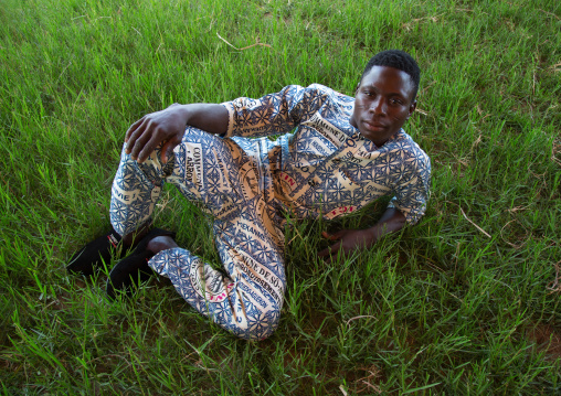Benin, West Africa, Ganvié, fashionable young man in traditional beninese clothing resting in a field