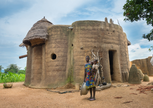 Benin, West Africa, Boukoumbé, mother and her baby in front of her traditional tata somba house with thatched roofs and granaries