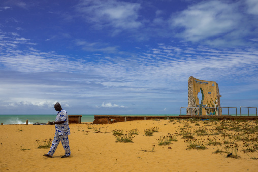Benin, West Africa, Ouidah, man passing in front of the memorial of the grand jubilee of 2000