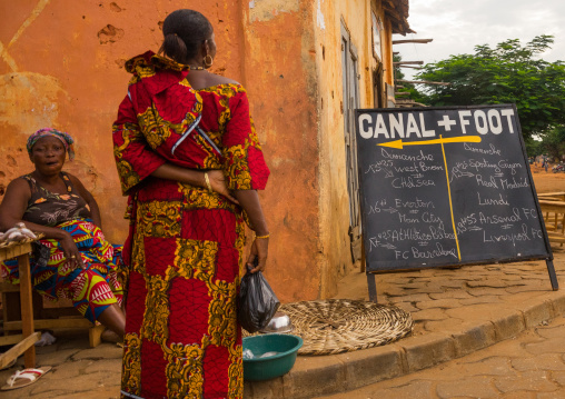 Benin, West Africa, Ouidah, women in the street in front of a canal plusfootball billboard