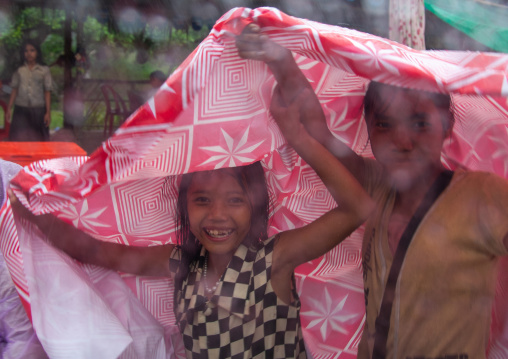 Cambodian children protecting themselves from the rain with a tablecloth, Siem Reap Province, Angkor, Cambodia