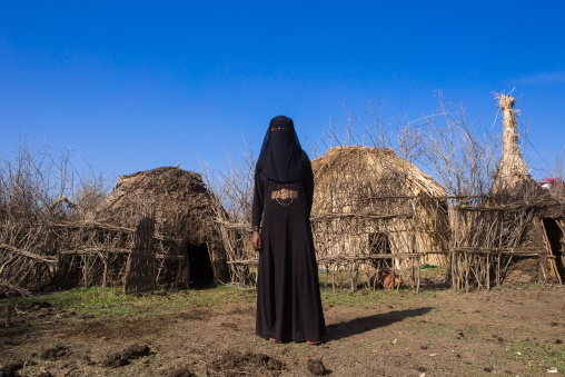 An ethiopian oromo woman dressed in black burqa stands in front of her hut, Amhara region, Artuma, Ethiopia