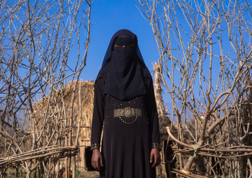An ethiopian oromo woman dressed in black burqa stands in front of her hut, Amhara region, Artuma, Ethiopia
