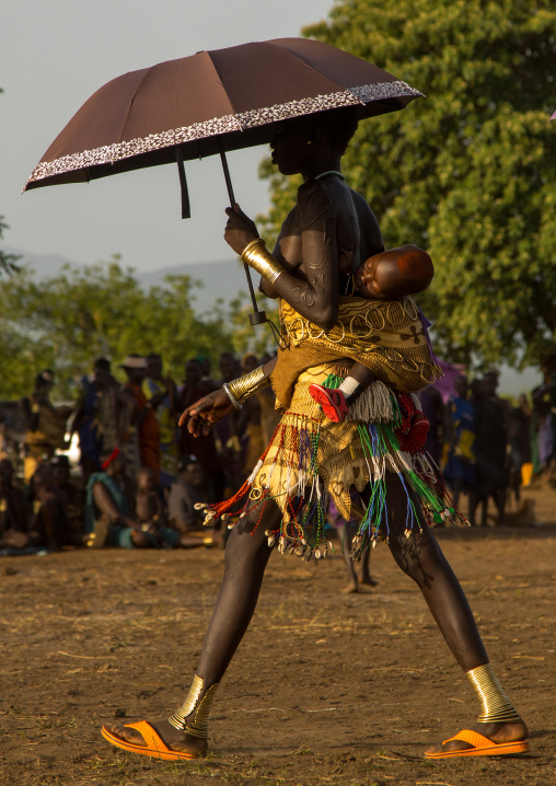 Woman carrying her baby on her back with an umbrella during the fat men ceremony in Bodi tribe, Omo valley, Hana Mursi, Ethiopia