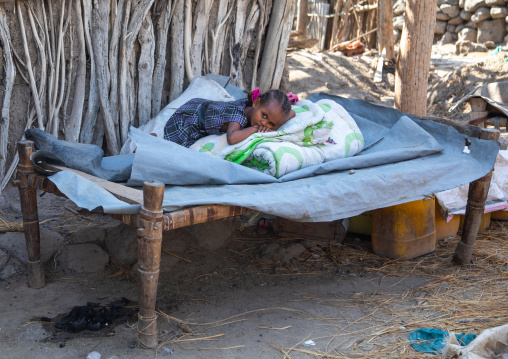 Ethiopian girl resting on a bed in front of her house, Afar Region, Assayta, Ethiopia
