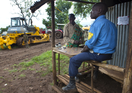 Policeman And Man From Koka Malaysian Plantation Playing Checkers Near Bulldozers, Omo Valley, Ethiopia
