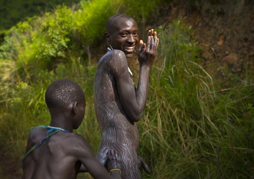Shepherd from Suri tribe receiving help to decorate his body with camouflage paintings, Tulgit, Omo valley, Ethiopia