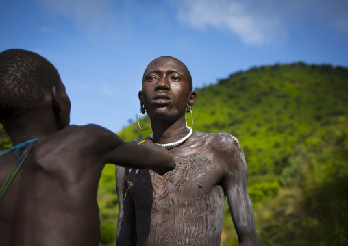 Shepherd from Suri tribe receiving help to decorate his body with camouflage paintings, Tulgit, Omo valley, Ethiopia