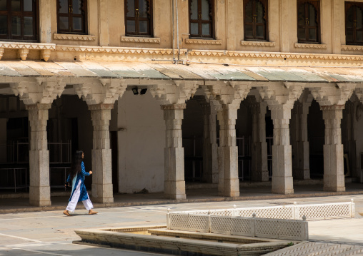 Indian woman walking under arches in the city palace, Rajasthan, Udaipur, India