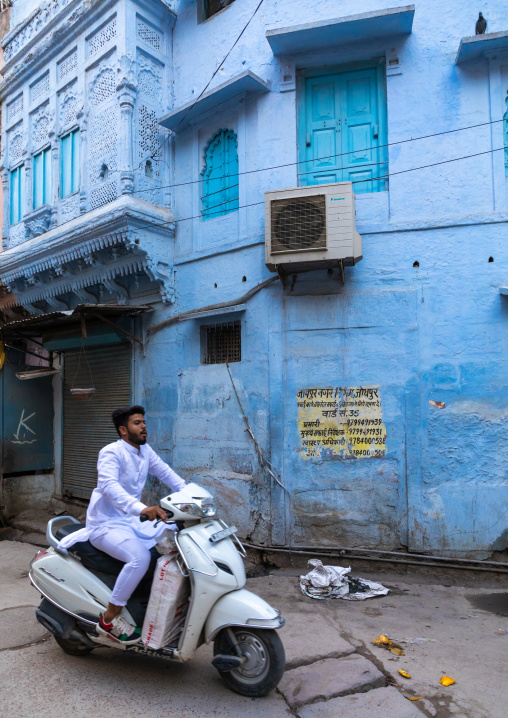 Indian man passing by an old blue house of a brahmin in scooter, Rajasthan, Jodhpur, India