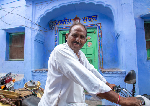 Indian man riding a mototbike in front of a old blue house of a brahmin, Rajasthan, Bundi, India