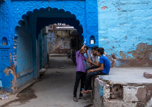 Indian young men sit at the entrance of an old blue house of a brahmin, Rajasthan, Jodhpur, India
