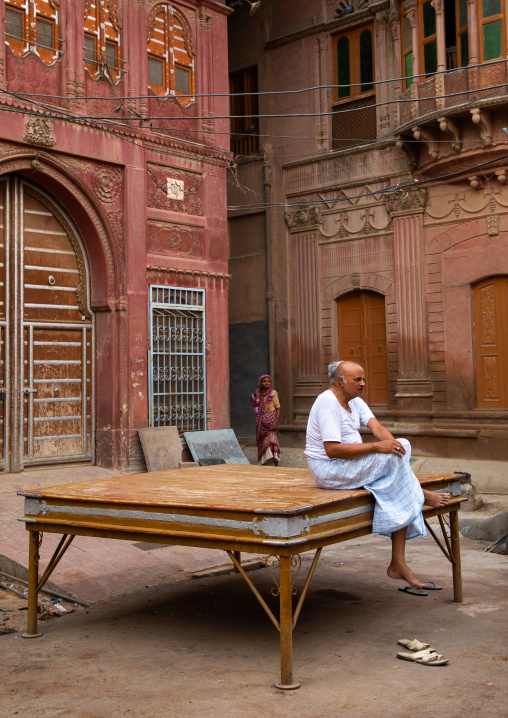 Indian man sit on a resting bed in front of a beautiful haveli in the old city, Rajasthan, Bikaner, India
