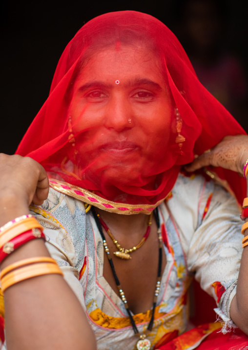 Portrait of a rajasthani woman hidding her face under a red sari, Rajasthan, Jaisalmer, India