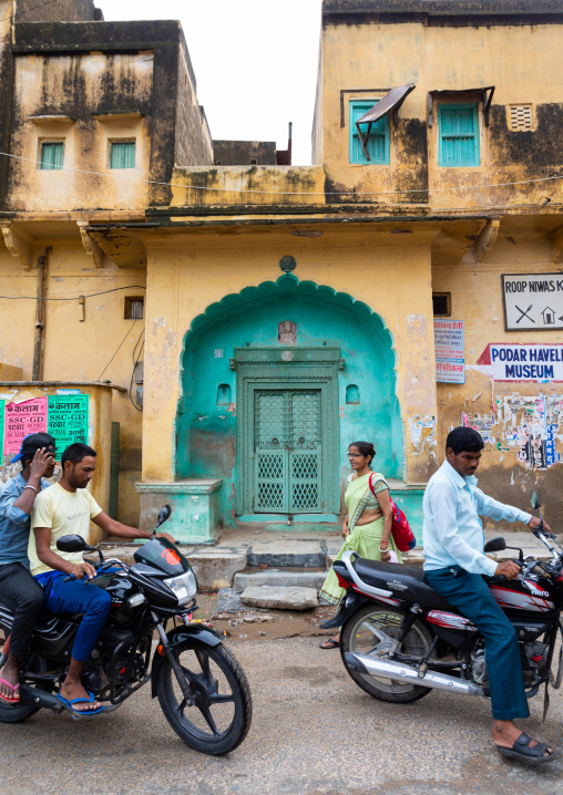 Indian people on motorbikes passing by an old historic haveli, Rajasthan, Nawalgarh, India