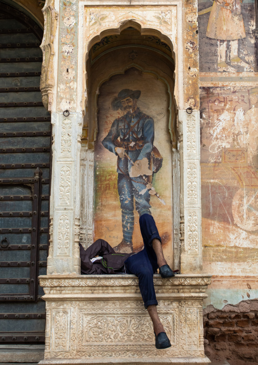 Indian man sleeping under a wall painting of an old haveli, Rajasthan, Nawalgarh, India