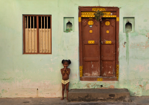 Little Girl With Hands Over The Mouth Posing In Front Of A House In Pondichery, India
