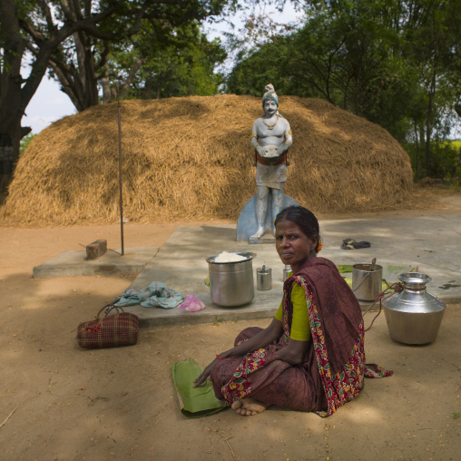 Woman Sitting On The Ground Preparing Food In Front Of A Hindu Statue And A Haystack, Pondicherry, India