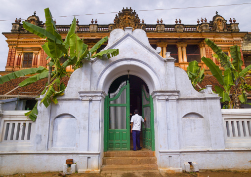 Man Opening The Portal Of A Old Chettiar Mansion With Banana Trees And Carvings Of Hindu Image, Kanadukathan Chettinad, India