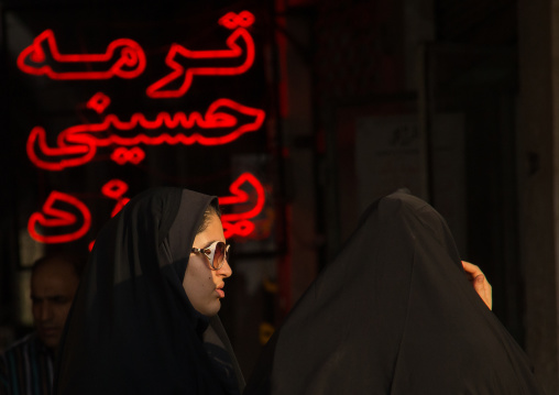 veiled women in front of red neon lights, Central district, Tehran, Iran