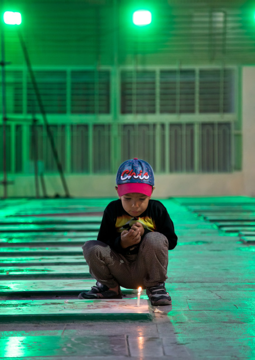 Portrait of an iranian shiite boy putting a candle on a tomb in the rose garden of martyrs cemetery, Isfahan Province, Isfahan, Iran