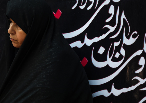 Iranian shiite woman in front of a billboard with calligraphy during Muharram to commemorate the martyrdom anniversary of Hussein, Lorestan Province, Khorramabad, Iran