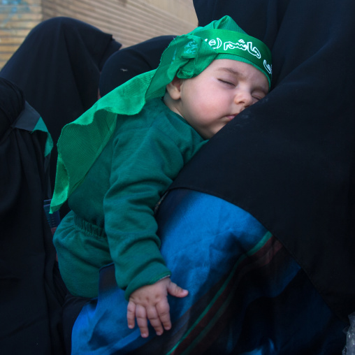 Iranian shiite muslim baby dressed for Muharram and sleeping on her mother shoulder, Lorestan Province, Khorramabad, Iran