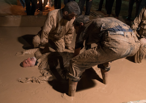 An iranian shiite muslim man rolls over in a mud pond as he takes part in the Kharrah Mali ritual during the Ashura ceremony, Lorestan Province, Khorramabad, Iran