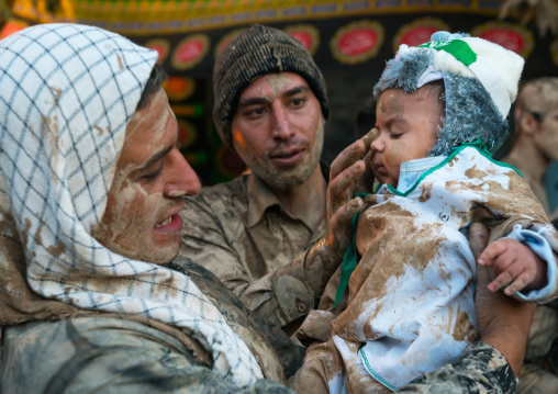 Iranian shiite muslim men rubbing mud on a baby during the Kharrah Mali ritual to mark the Ashura day, Lorestan Province, Khorramabad, Iran